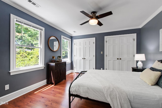 bedroom featuring two closets, crown molding, wood finished floors, baseboards, and ceiling fan