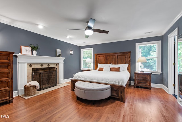 bedroom with wood finished floors, ornamental molding, a fireplace, a ceiling fan, and baseboards
