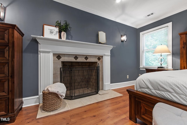 bedroom with wood finished floors, a fireplace, ornamental molding, and baseboards