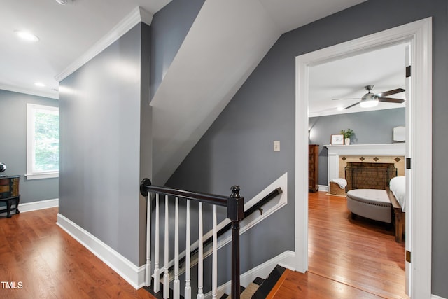 hallway with an upstairs landing, ornamental molding, wood finished floors, baseboards, and recessed lighting