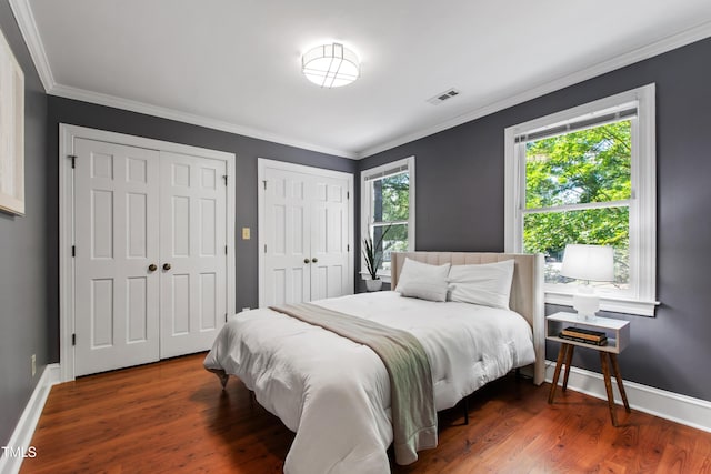 bedroom with multiple closets, crown molding, wood finished floors, and baseboards