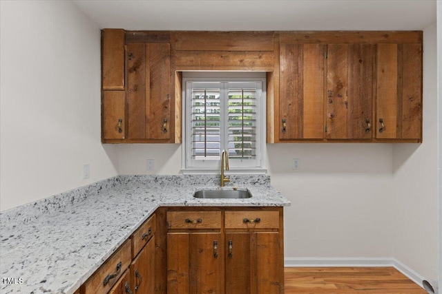 4713 Erwin Rd, Durham, NC 27705 - kitchen featuring a sink, brown cabinets, wood finished floors, light stone counters, and baseboards