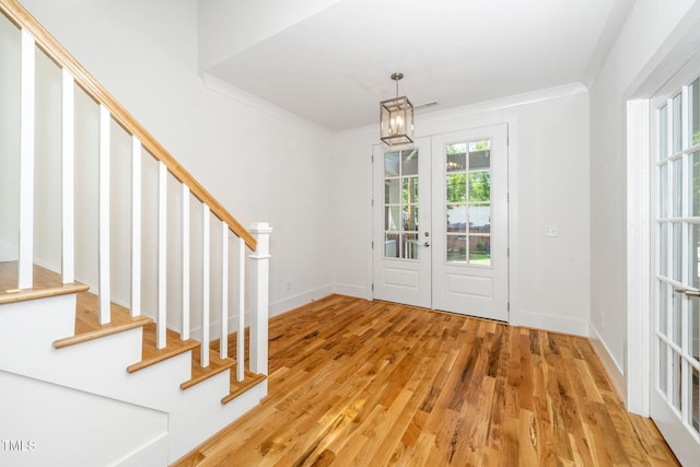 foyer entrance featuring stairs, light wood-style flooring, ornamental molding, french doors, and a chandelier