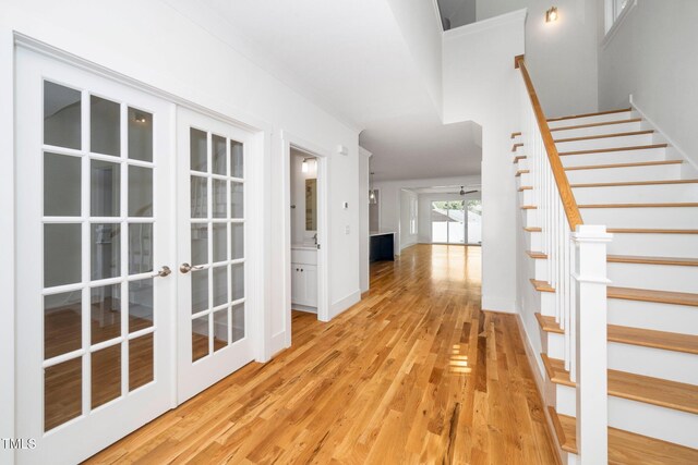 hallway featuring stairway, light wood-style floors, and french doors