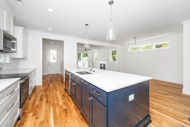 kitchen featuring stainless steel appliances, a sink, white cabinetry, blue cabinetry, and light countertops