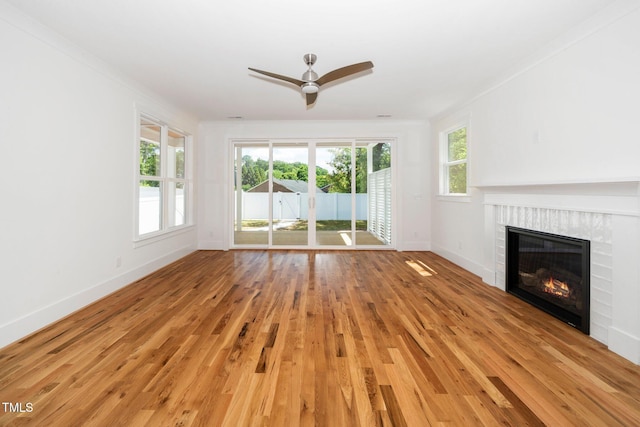 unfurnished living room with baseboards, ceiling fan, light wood-style flooring, a fireplace, and crown molding