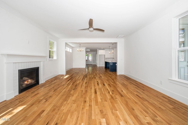 unfurnished living room featuring a chandelier, light wood-style flooring, a fireplace, a ceiling fan, and baseboards