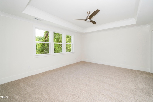 spare room with a tray ceiling, light carpet, ceiling fan, ornamental molding, and baseboards