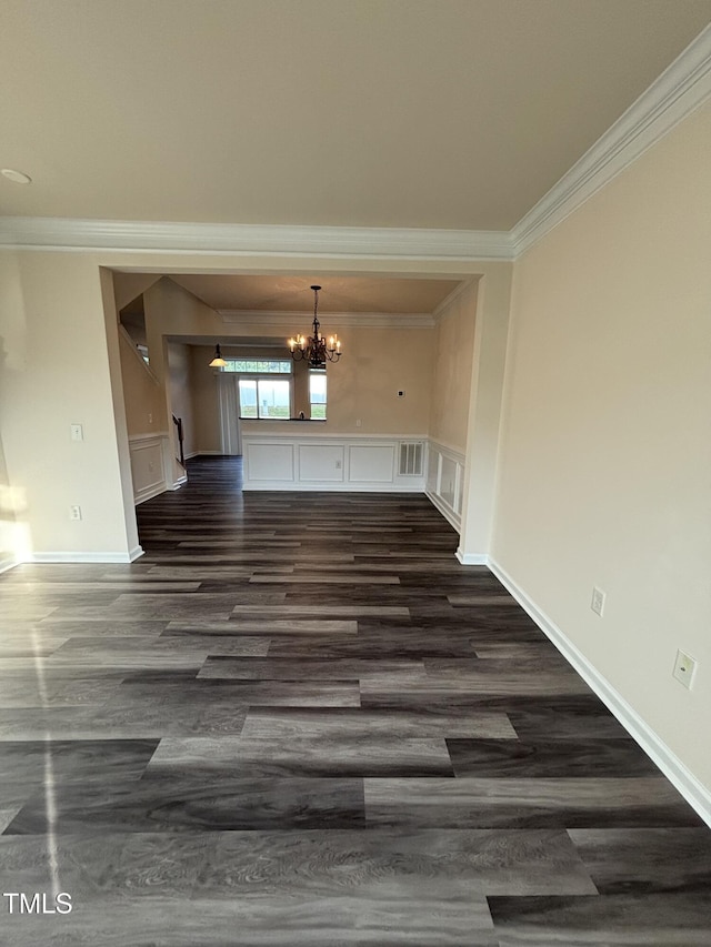 unfurnished dining area featuring crown molding, dark wood-type flooring, a chandelier, a wainscoted wall, and a decorative wall
