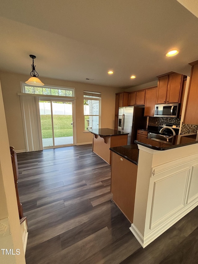 kitchen with appliances with stainless steel finishes, dark wood-style floors, dark countertops, brown cabinetry, and recessed lighting