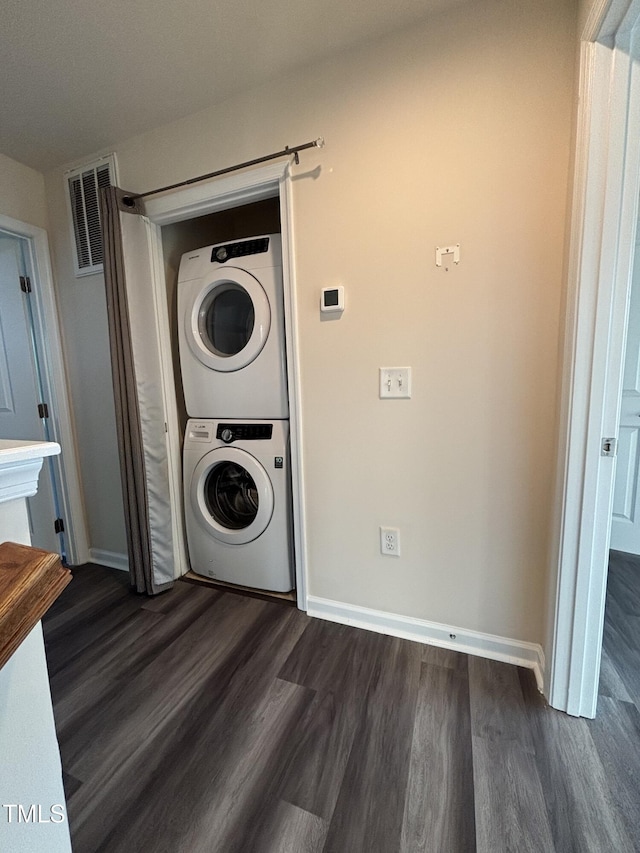 clothes washing area with stacked washer / drying machine, dark wood-style flooring, and baseboards