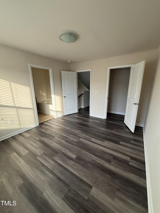 unfurnished bedroom with dark wood finished floors, baseboards, a walk in closet, and ensuite bath