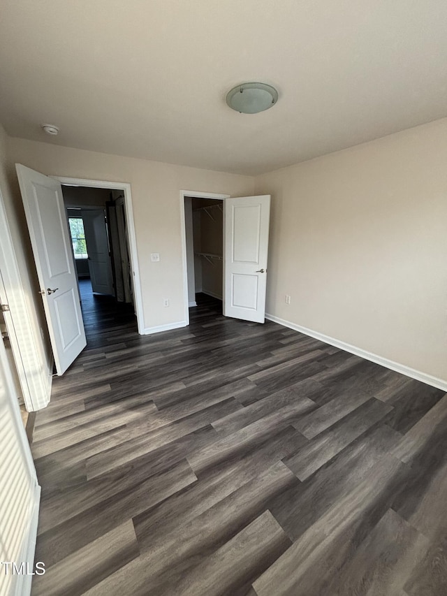 unfurnished bedroom featuring baseboards, dark wood-style floors, and a closet