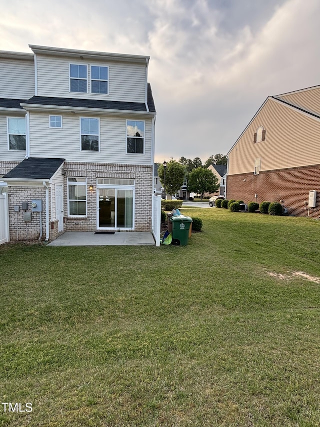 rear view of house featuring a patio, a lawn, and brick siding