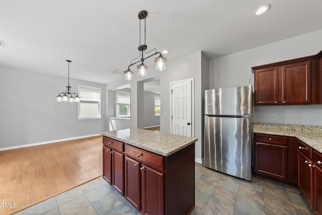 kitchen with freestanding refrigerator, pendant lighting, a kitchen island, light stone counters, and recessed lighting