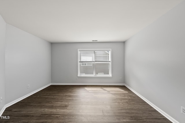 spare room featuring dark wood-type flooring and baseboards
