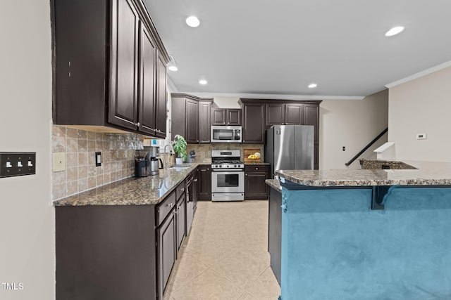 kitchen with stainless steel appliances, a sink, dark brown cabinetry, a kitchen bar, and backsplash