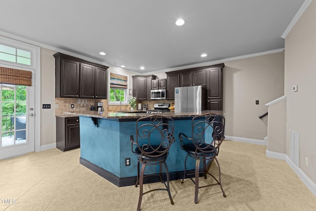 kitchen featuring stainless steel appliances, ornamental molding, decorative backsplash, a breakfast bar, and dark stone counters
