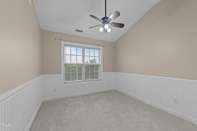 spare room with a wainscoted wall, lofted ceiling, a ceiling fan, and carpet