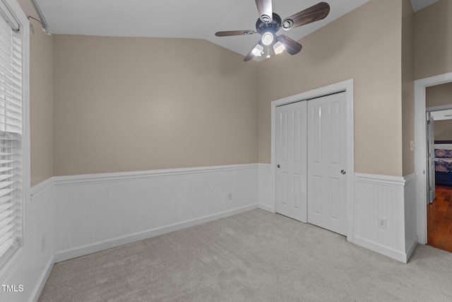 unfurnished bedroom with a wainscoted wall, lofted ceiling, carpet floors, a closet, and a ceiling fan