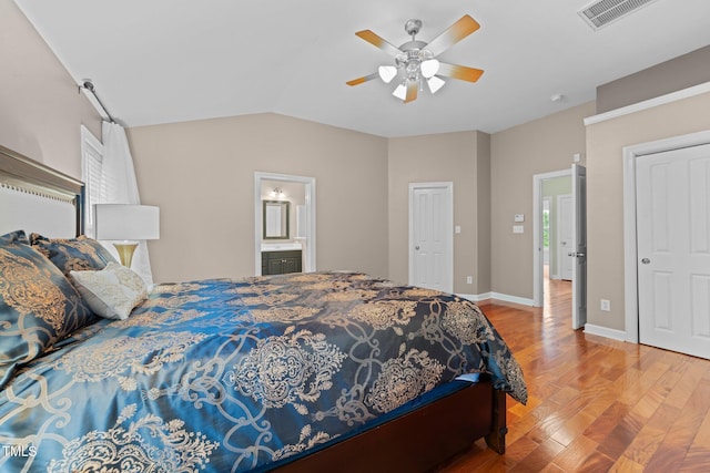bedroom with wood finished floors, a ceiling fan, vaulted ceiling, baseboards, and connected bathroom