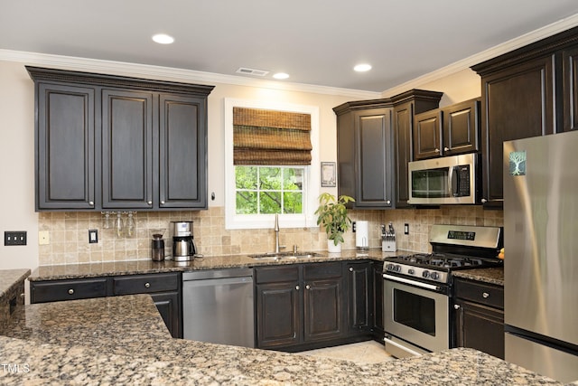 kitchen with appliances with stainless steel finishes, a sink, dark stone counters, ornamental molding, and backsplash