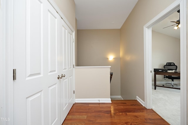 hall with an upstairs landing, wood finished floors, baseboards, and an office area