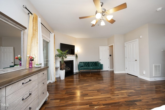 unfurnished room featuring dark wood finished floors, a ceiling fan, a fireplace with flush hearth, and baseboards