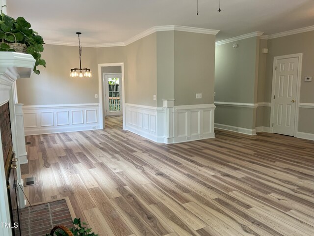 8100 Laurel Mountain Rd, Raleigh, NC 27613 - empty room featuring light wood-style floors, a chandelier, crown molding, a fireplace, and a wainscoted wall