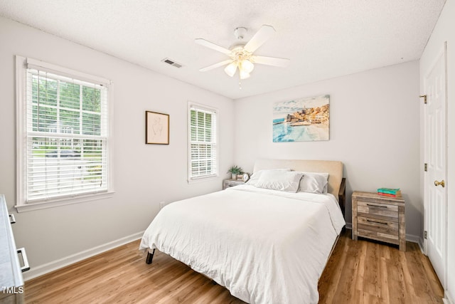 bedroom with multiple windows, light wood finished floors, baseboards, ceiling fan, and a textured ceiling