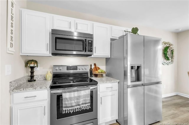 6955 S W St, Godwin, NC 28344 - kitchen with appliances with stainless steel finishes, white cabinets, light stone counters, light wood finished floors, and baseboards