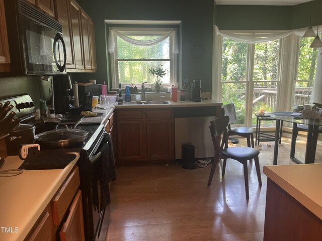 kitchen with a sink, black appliances, light wood-style floors, light countertops, and brown cabinetry