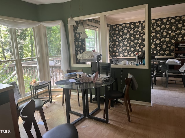 dining space featuring ornamental molding, wallpapered walls, and wood finished floors