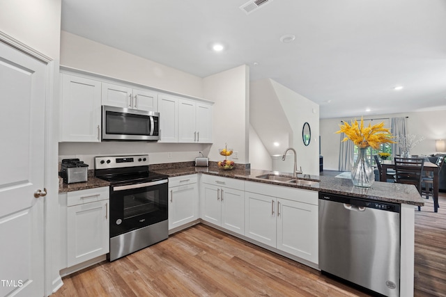 4157 Trevino Dr, Durham, NC 27704 - kitchen with stainless steel appliances, a sink, a peninsula, dark stone countertops, and light wood-type flooring