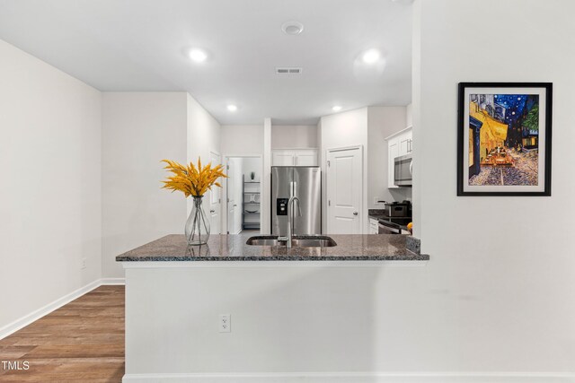 4157 Trevino Dr, Durham, NC 27704 - kitchen with appliances with stainless steel finishes, a peninsula, dark stone counters, white cabinets, and a sink