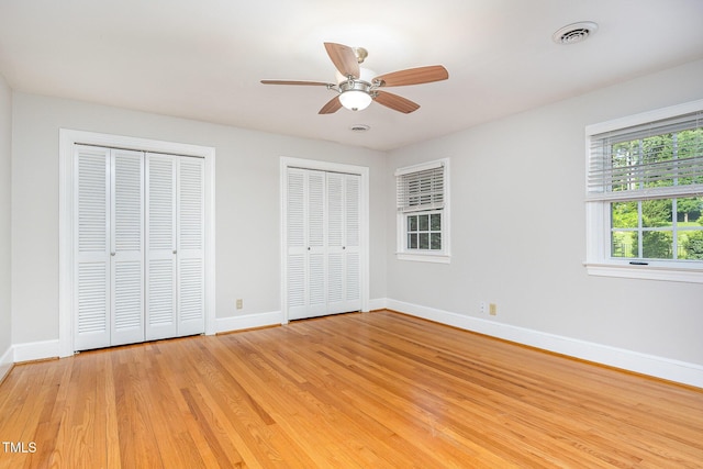 unfurnished bedroom with two closets, baseboards, light wood finished floors, and a ceiling fan