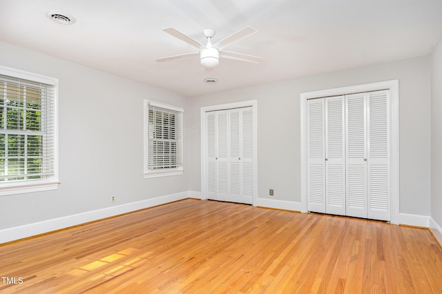unfurnished bedroom with multiple closets, light wood-style floors, baseboards, and a ceiling fan