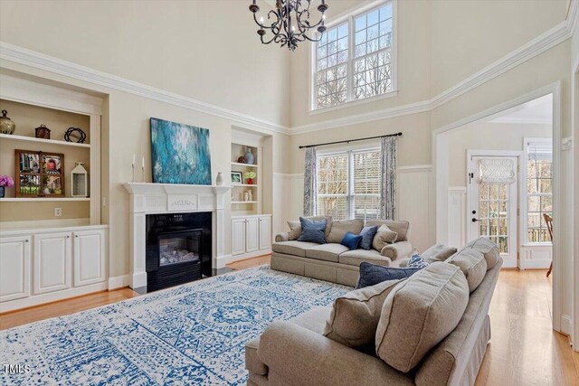 living area featuring built in features, a high ceiling, light wood-style flooring, a chandelier, and a fireplace with flush hearth