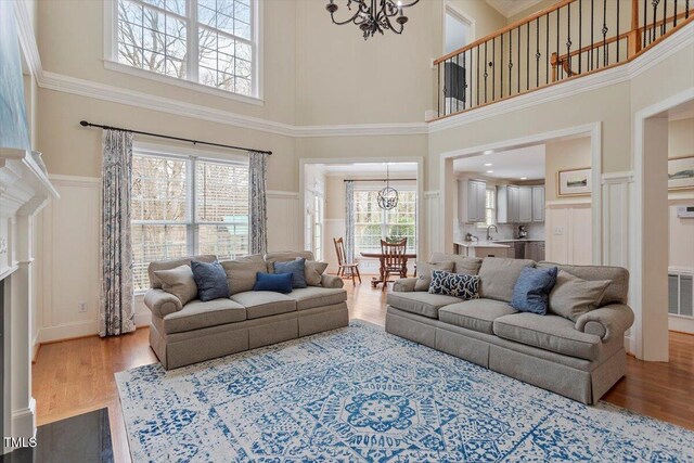living room featuring a towering ceiling, a chandelier, a decorative wall, wood finished floors, and wainscoting