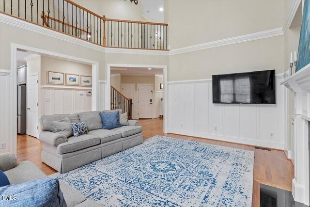 living area with stairs, a towering ceiling, wood finished floors, a decorative wall, and a wainscoted wall