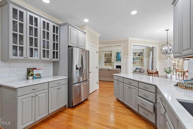 kitchen featuring gray cabinetry, stainless steel fridge, crown molding, glass insert cabinets, and light wood-type flooring