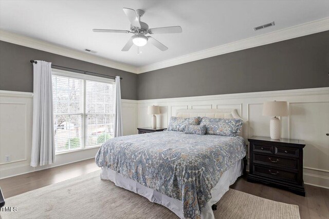 bedroom with wood finished floors, crown molding, wainscoting, and a ceiling fan