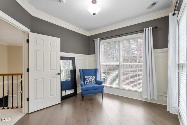 living area featuring wainscoting, wood finished floors, crown molding, and a decorative wall