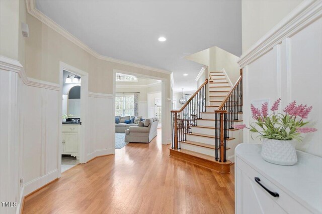 entrance foyer featuring stairway, light wood-type flooring, ornamental molding, and a decorative wall