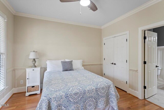 bedroom featuring light wood-type flooring, ornamental molding, multiple windows, wainscoting, and a closet