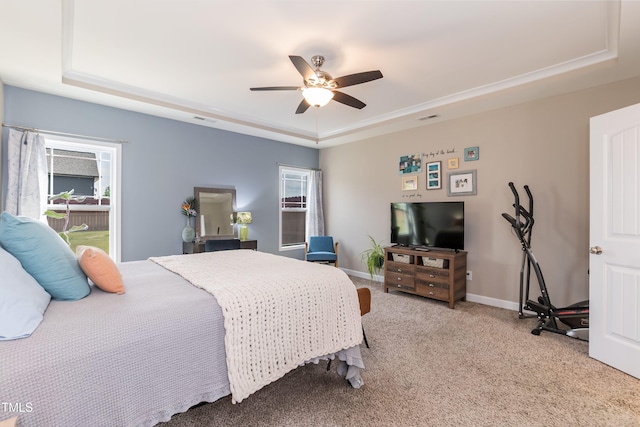 carpeted bedroom featuring a tray ceiling, multiple windows, baseboards, and a ceiling fan