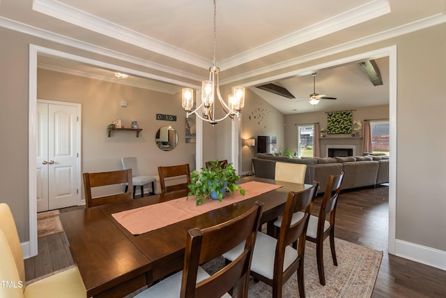 dining room featuring a ceiling fan, a tray ceiling, dark wood finished floors, a fireplace, and crown molding