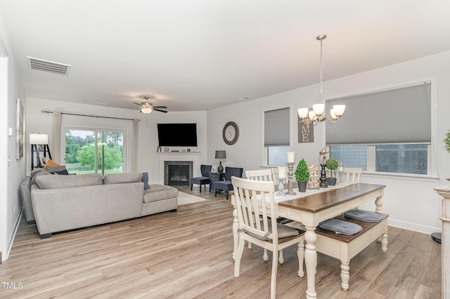 646 Shelford Trl, Zebulon, NC 27597 - dining area featuring a glass covered fireplace, light wood finished floors, a ceiling fan, and a chandelier