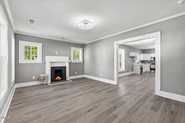 unfurnished living room with crown molding, wood finished floors, baseboards, and a brick fireplace