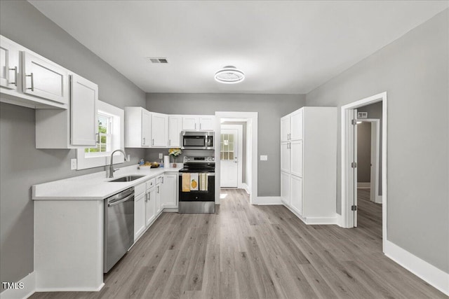 kitchen with appliances with stainless steel finishes, a sink, white cabinetry, light wood finished floors, and light countertops
